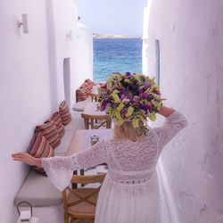 Rear view of woman wearing flowers while walking in alley against sea