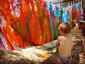 Rear view of shirtless boy coloring textile