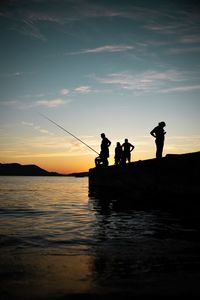 Silhouette people on pier over lake against sky during sunset