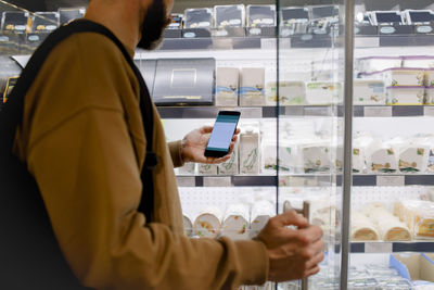 Midsection of male customer using smart phone while shopping in supermarket