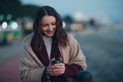 Portrait of smiling young woman using phone while standing outdoors