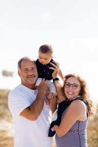 Grandparents smiling & holding grandson on beach