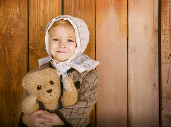 Portrait of smiling girl holding toy against wooden wall