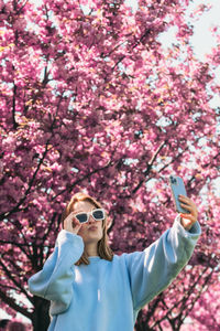 Portrait of young woman wearing sunglasses while standing against trees