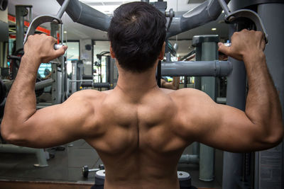 Rear view of shirtless man exercising in gym