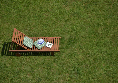 Wooden easy chair on a garden lawn, with cushions, book, sunglasses and a hat