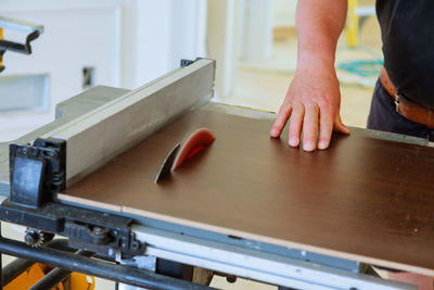 Midsection of worker cutting plank with saw in workshop