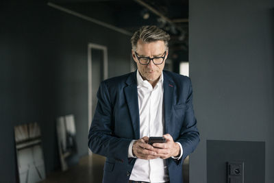 Mature businessman standing in office using cell phone