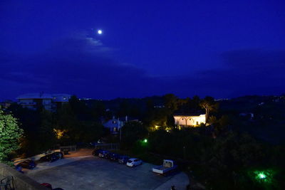 Illuminated street amidst buildings against sky at night