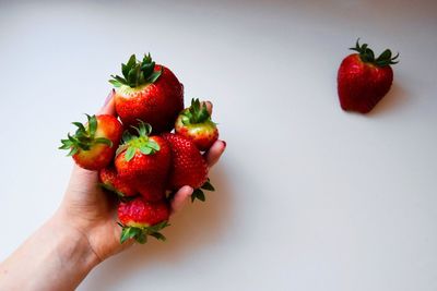 Close-up of cropped hand holding strawberry over white background