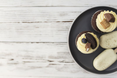 White cookie ice creams on a stick and tasty muffins and cupcakes on a tray on a wooden background