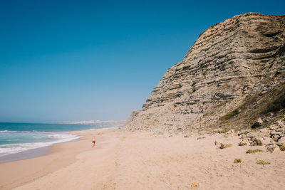 Rock formations at beach against blue sky