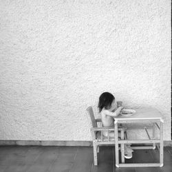 Rear view of woman sitting on chair against wall