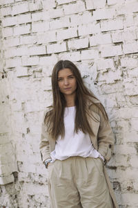 Portrait of smiling young woman standing against brick wall