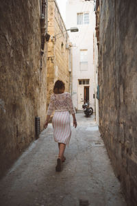 Rear view of woman walking on narrow street amidst buildings