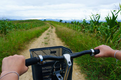 Cropped image of man riding bicycle on road amidst field against sky