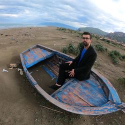 Portrait of man sitting in boat on sand against sky