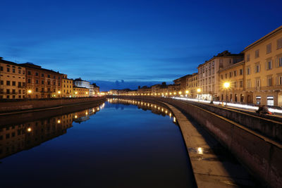 Illuminated buildings by river against blue sky at night