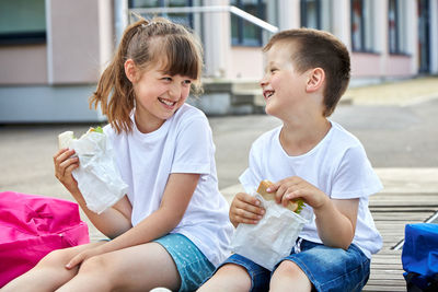 Schoolchildren boy and girl laugh and eat their lunch, snack, breakfast in the school yard. 