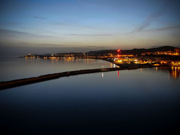 Illuminated city by river against sky at night