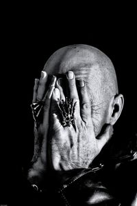 Close-up of senior man covering face with hand against black background