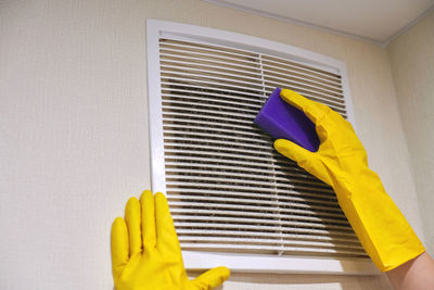 Hands in protective rubber gloves cleaning dusty air ventilation grill of hvac. cleaning service