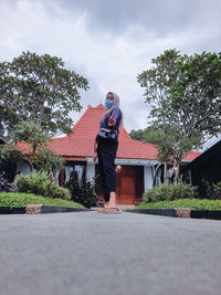 Man standing by house against sky