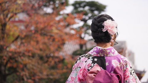 Rear view of woman with pink flowers against blurred background