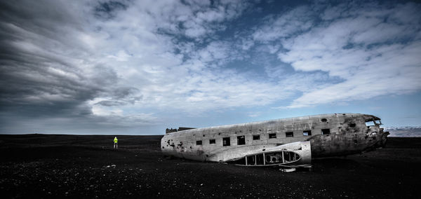 Person by airplane wreckage on field against cloudy sky