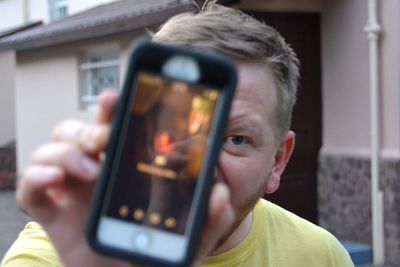 Close-up portrait of man showing mobile phone screen outdoors