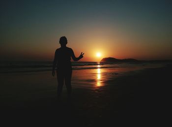 Silhouette person gesturing peace sign while standing at beach during sunset