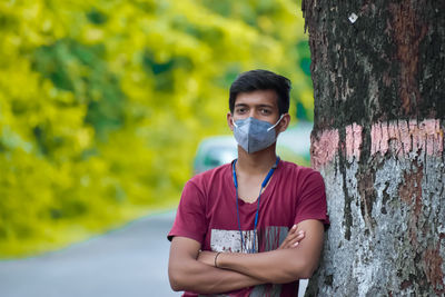 Portrait of young man standing against tree trunk