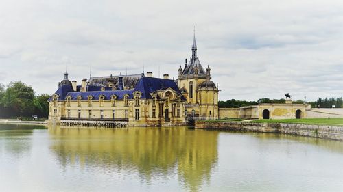 View of buildings by river against cloudy sky