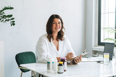 Young smiling brunette woman nutritionist plus size in white shirt working at laptop on table 