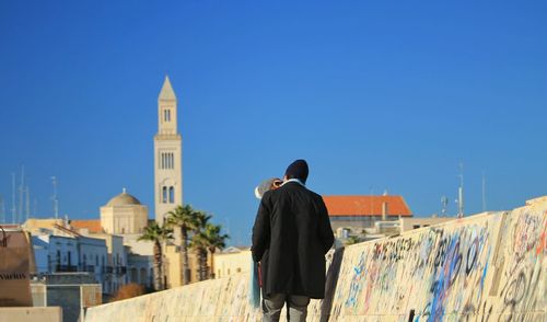 Rear view of people looking at city buildings against blue sky