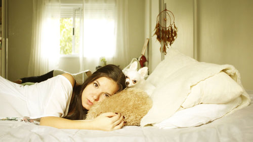 Portrait of young woman relaxing with dog on bed at home