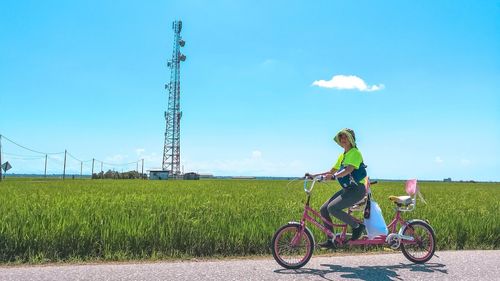 Woman riding bicycle on field against sky