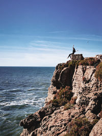 Woman sitting on mountain by sea against sky