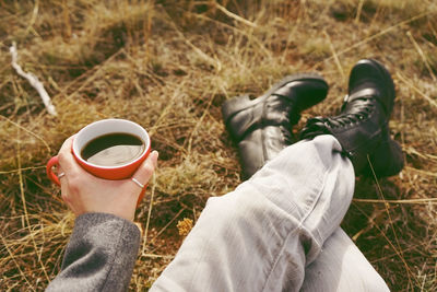 Low section of person holding coffee cup on field