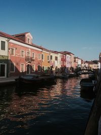 Boats moored on canal in city against clear sky