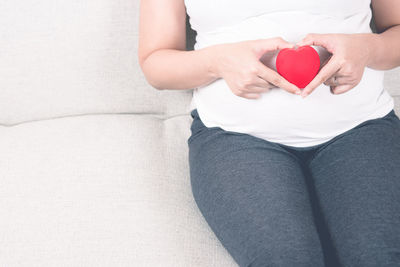 Midsection of pregnant woman with heart shape sitting on sofa 