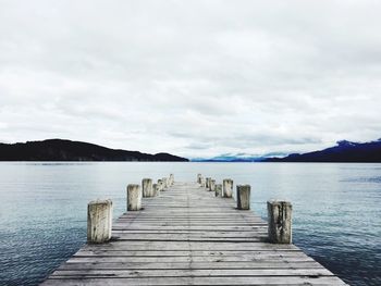 Jetty at lake against cloudy sky