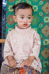 Portrait of cute baby girl with flag make up on her cheeks with traditional clothes as background 