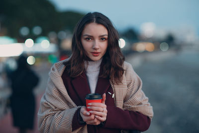 Portrait of young woman standing against wall during winter