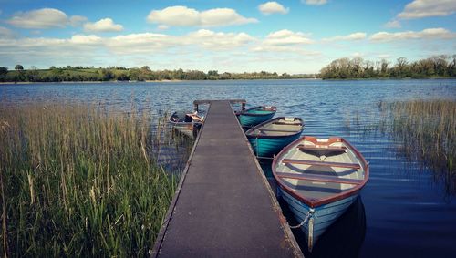 Boats moored by pier at lake against sky