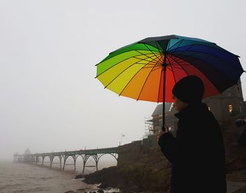 Teenage boy holding umbrella while standing against sea during foggy weather