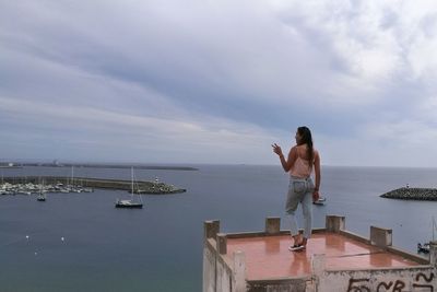 Woman standing on building terrace against sea against sky