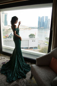 Rear view of woman standing by window at home