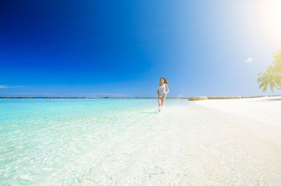 Full length of woman on beach against blue sky