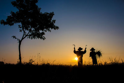 Silhouette farmers harvesting on field against sky during sunset